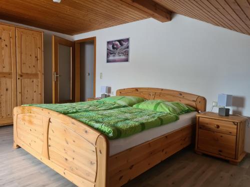 a wooden bed with a green comforter in a bedroom at Ferienwohnung Huber am Deutensee in Steingaden