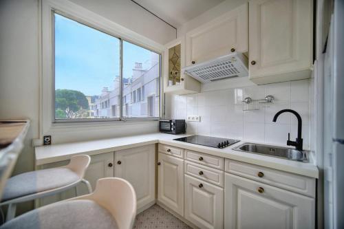 une cuisine avec des armoires blanches, un évier et une fenêtre dans l'établissement IMMOGROOM - Cosy - Californie - Proximité de tout, à Cannes