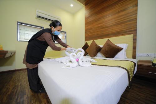 Una mujer con una máscara haciendo una cama con un animal de peluche. en Vijaya Tej Clarks Inn, en Patna