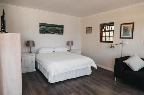 a white bedroom with a bed and a chair at Mitre's Edge Vineyard Studio in Klapmuts