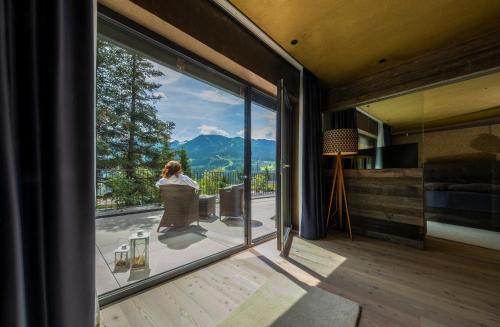 a woman standing on a balcony looking out the window of a house at La Roccia Wellness Hotel in Cavalese