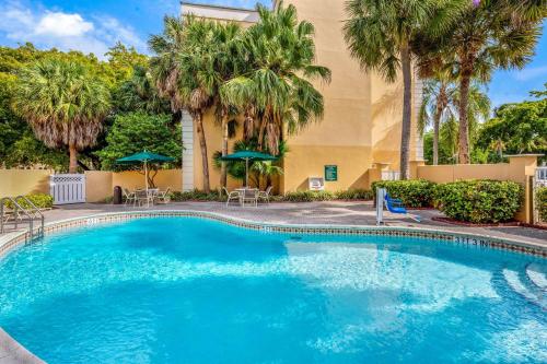 a swimming pool with palm trees and a building at La Quinta by Wyndham Miami Lakes in Miami Lakes