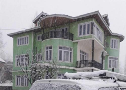 een groen en wit huis met sneeuw erop bij Calm Holiday Inn in Srinagar