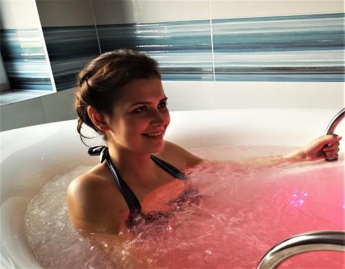 a woman is sitting in a bathtub with pink water at Ośrodek Uzdrowiskowy Świerkowy Zdrój Medical Spa in Rymanów-Zdrój