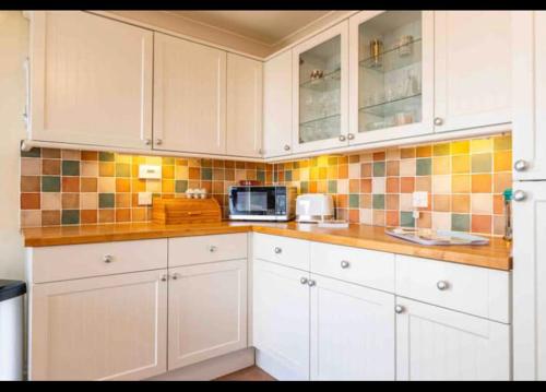 a kitchen with white cabinets and a microwave at Fantastic spacious house with beautiful panoramic views of the bay Only a few minutes walk from beach harbour and restaurants This house has 3 bedrooms 3 bathrooms and 2 lovely sitting rooms in Lyme Regis