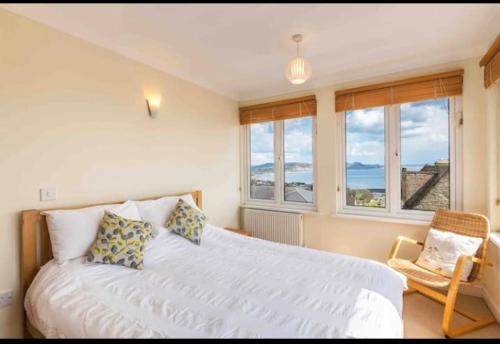 a bedroom with a bed and a chair and windows at Fantastic spacious house with beautiful panoramic views of the bay Only a few minutes walk from beach harbour and restaurants This house has 3 bedrooms 3 bathrooms and 2 lovely sitting rooms in Lyme Regis