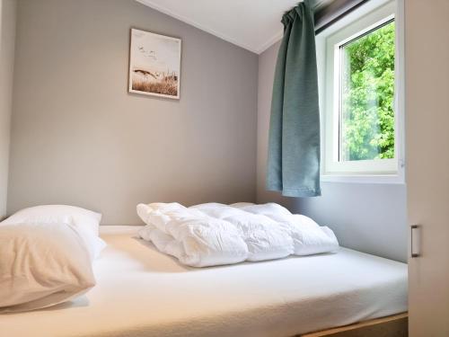 a bedroom with a bed with white sheets and a window at Nieuw! OK40 Landelijk gelegen Chalet in Oostkapelle