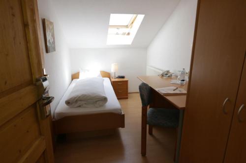 a small bedroom with a bed and a desk and a window at Landgasthof Pauliwirt in Erharting