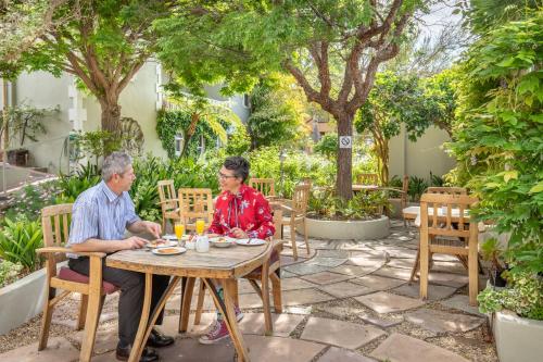 zwei ältere Menschen sitzen an einem Tisch in einem Garten in der Unterkunft Montagu Country Hotel in Montagu