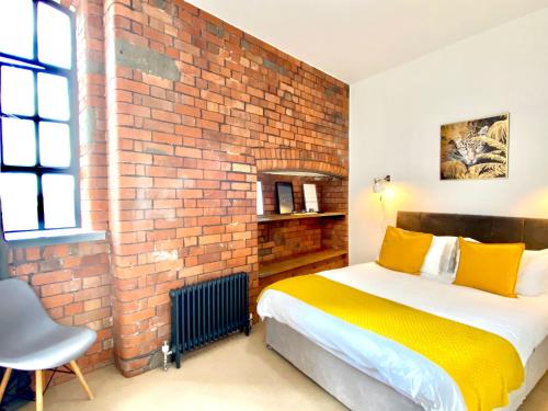 Un dormitorio con una pared de ladrillo y una cama con almohadas amarillas. en Victorian Factory Apartment with 2 Bedrooms en Bristol
