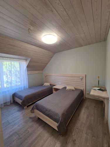 two beds in a room with a wooden ceiling at Viesu nams UPE in Roja