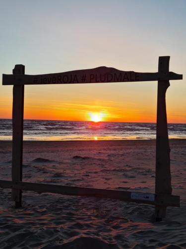 a wooden sign on the beach with the sunset in the background at Viesu nams UPE in Roja