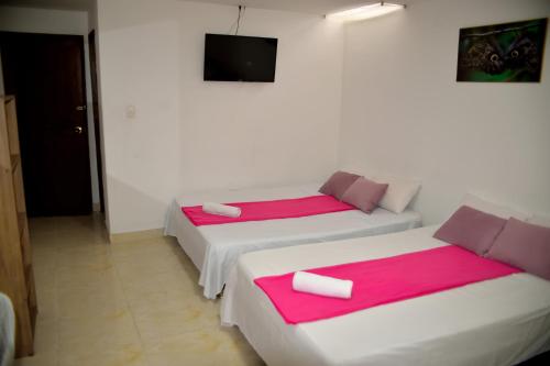 two beds in a white room with pink sheets at Hotel Casa Alejandria in Quimbaya