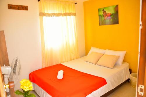 a bedroom with a bed with an orange blanket and a window at Hotel Casa Alejandria in Quimbaya