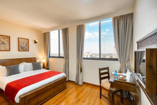 a hotel room with a bed and a desk and windows at Kibo Palace Hotel Moshi in Moshi
