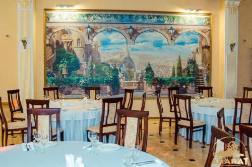 a dining room with tables and chairs in front of a painting at Hotel Ararat in Lermontov