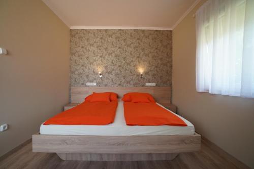a bedroom with a bed with orange sheets and a window at Tavi Panzió in Dunapataj