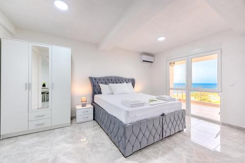 a white bedroom with a bed and a large window at Apartmani Panorama in Bar