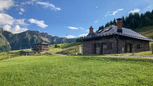an old stone house in a field with mountains in the background at Baita Casera Caviazza in Falcade