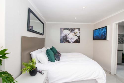 a white bedroom with a white bed with green pillows at Prestigious Apartments in Fourways