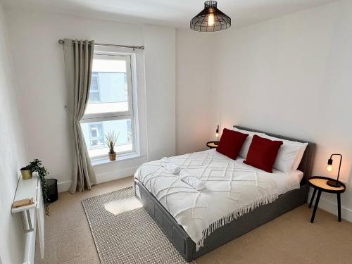 a bedroom with a bed with red pillows and a window at 2 Bedroom Serviced Apartment with Free Parking, Wifi & Netflix, Basingstoke in Basingstoke
