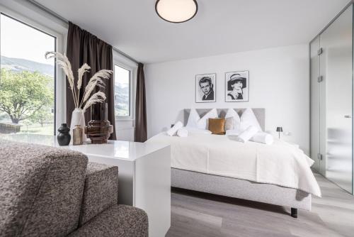 a white bedroom with a bed and a chair at Max Studios & Apartments - Zillertal in Schlitters