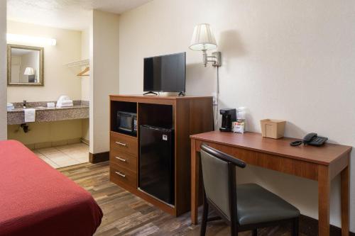 a hotel room with a desk with a television and a bed at Americana Inn a Travelodge by Wyndham in Pigeon Forge