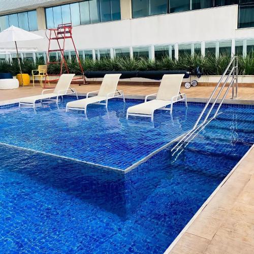 a pool with chairs and a swing in a building at True América apart-hotel in Campos dos Goytacazes