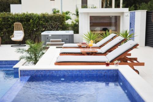 a pool with chaise lounge chairs next to a swimming pool at Villa Pino with Pool, Sauna & Jacuzzi in Petrcane