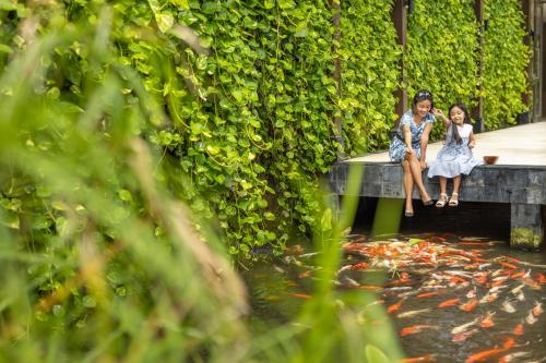 a man and woman sitting on a bench next to a pond at The Seminyak Beach Resort & Spa in Seminyak