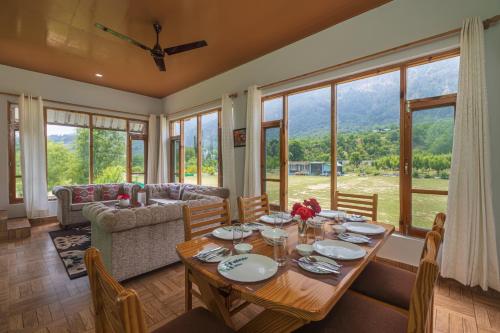 a dining room with a table and a couch at SaffronStays Persimmon House, Raison - luxury villa with Baes river and paragliding point views in Grāmag