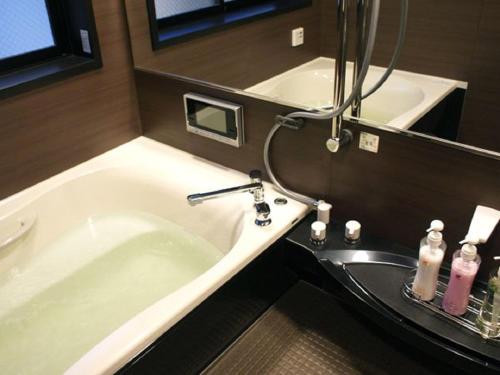 a bathroom with a bath tub and a sink at HOTEL LiVEMAX BUDGET Esaka in Suita