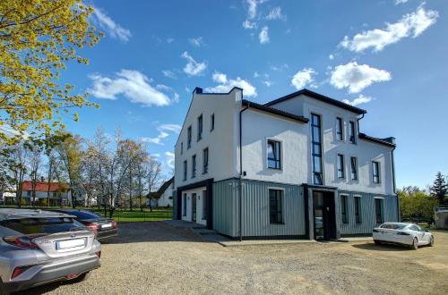 a white house with cars parked in a parking lot at Apartamentai Muzika in Šilutė