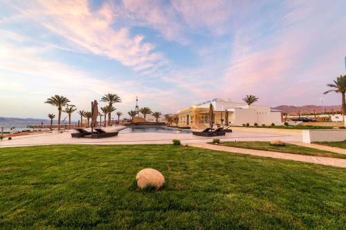 a field of grass with a building and palm trees at Luxotel Aqaba Beach Resort & Spa Only 15 years plus in Aqaba