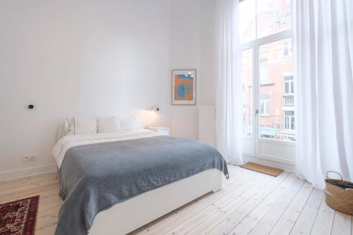 - une chambre blanche avec un lit et une grande fenêtre dans l'établissement Cosy and Modern 2 bedrooms flat near Châtelain and Brugmann, à Bruxelles