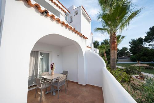 a patio with a table and chairs and a palm tree at Apartamentos Blanco Sol in Cala Vadella