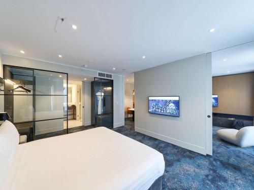 a bedroom with a white bed and a tv on a wall at Pullman Adelaide in Adelaide