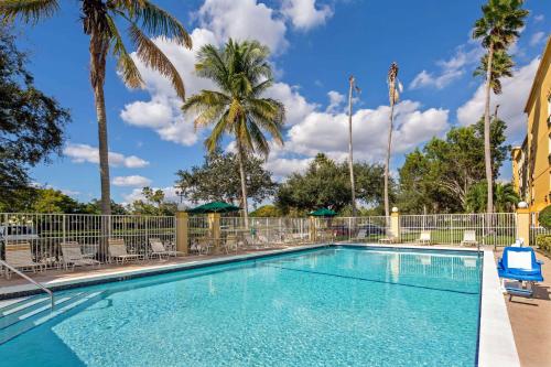 a swimming pool with chairs and palm trees at La Quinta Inn & Suites by Wyndham Sawgrass in Sunrise