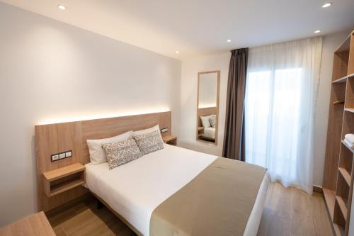 a bedroom with a large white bed and a window at Apartamentos Blanco Sol in Cala Vadella