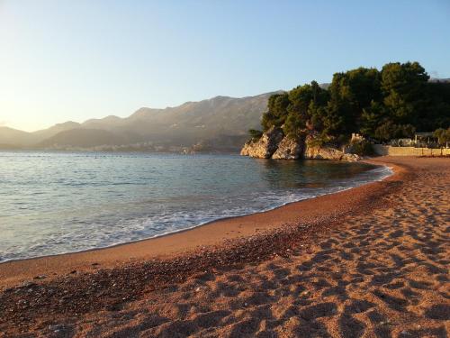 una playa de arena con el océano y las montañas en el fondo en Vila Horizont en Sveti Stefan