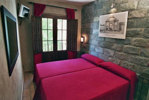 Una cama roja en una habitación con una pared de piedra. en Hospedería El Convento, en Estremera