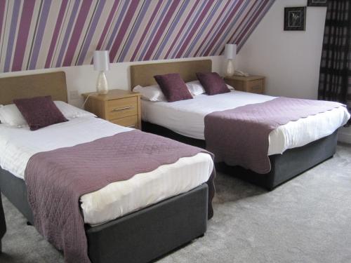 two beds in a hotel room with purple pillows at Glenburn Guest House in Windermere