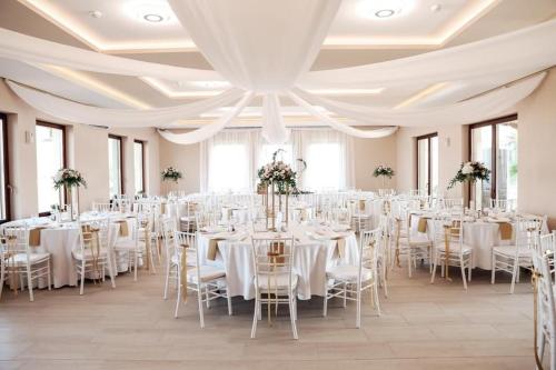 um salão de banquetes com mesas e cadeiras brancas em Auróra Rendezvényterem & Szállás em Jászapáti