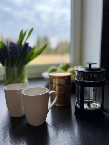 two cups and a coffee maker on a table with flowers at Stella in Ziemupe