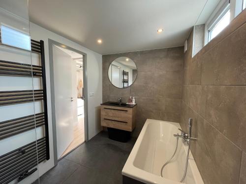 een badkamer met een bad, een wastafel en een spiegel bij Vakantiehuis Zeevonk Koudekerke in Koudekerke