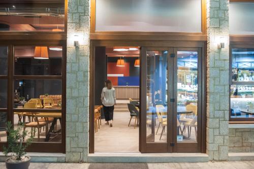a woman walks past a restaurant with tables and chairs at Parnassos Delphi Hotel in Delfoi