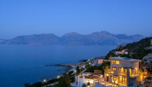 a house on a hill next to a body of water at Beachfront Villa Phi φ in Agios Nikolaos