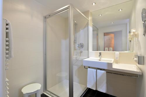 ein weißes Bad mit einer Dusche und einem Waschbecken in der Unterkunft Hotel Goldener Adler Wattens in Wattens
