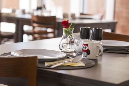 una mesa con platos y vasos y una rosa roja en un jarrón en Bałtycka44 Rooms & Apartments, en Olsztyn