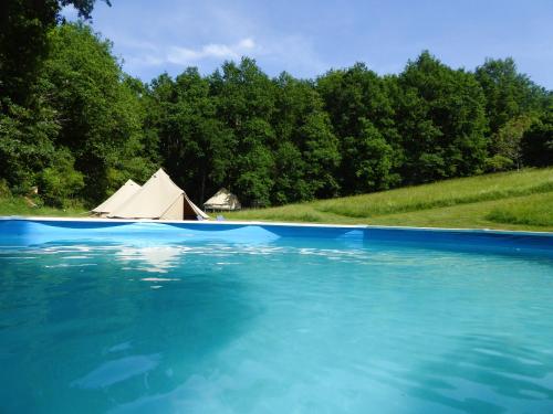 une piscine d'eau bleue avec une tente en arrière-plan dans l'établissement Belair le Camping, à Champagnac-de-Bélair